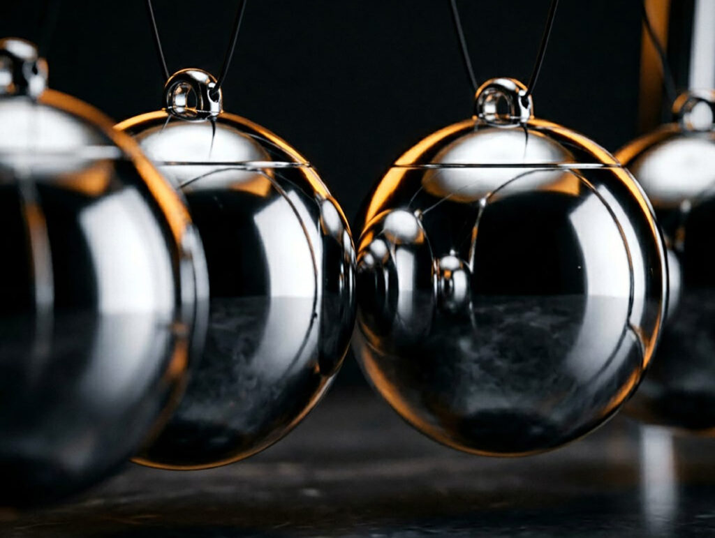 A row of polished metal balls in a Newton's cradle, one swinging to strike the line and set the others in motion — symbolizing emotional contagion and physiological synchrony, the article's central idea that a leader's state transmits through a team and sets everyone else's in motion.